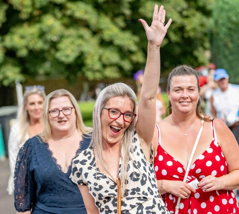 A race goer smiling for the camera with her hand in the air 