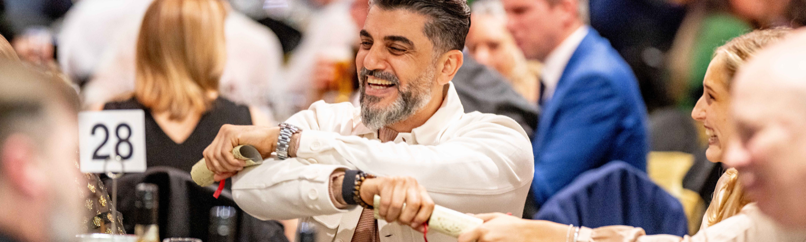 Man smiling as he crosses his arms to pull a cracker with friends at a Christmas Party.