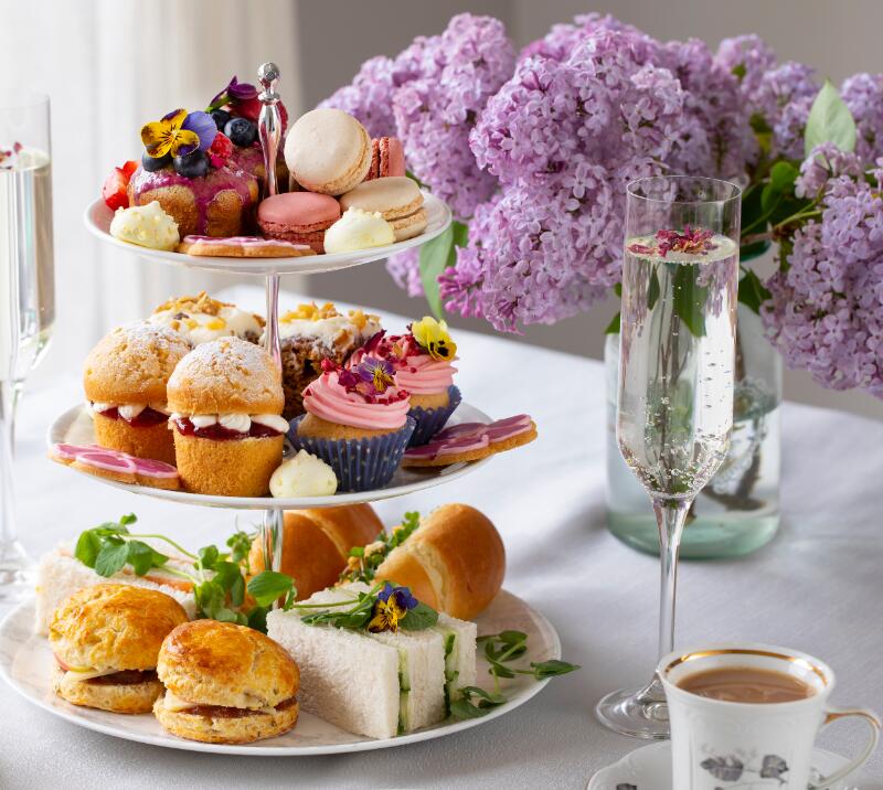 afternoon tea on tiered cake stand with cups of tea and glasses of champagne