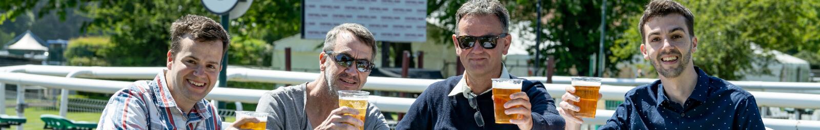 A group of smiling gentlemen sat at a table and chairs enjoying a beer in the sunshine
